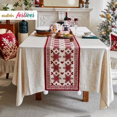 a dining room table with a christmas tree in the background and holiday decorations around it