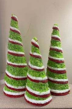 three small christmas trees made out of green grass and red trimmings on top of each other