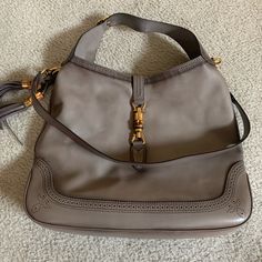 A Gucci Calfskin Duilio Brogue Large New Jackie Hobo Bag. This Gray Leather Bag Has A Removable Flat Leather Strap With Gold Tone Clasps And Anchors, A Flat Leather Adjustable Strap With Brogue Trim, Open Top With Gold Tone And Bamboo Style Piston Lock, Tassel Accent To One Side And Brogue Trim To The Top Lines And Along Base. The Interior Is Lined In Taupe Canvas With A Sidewall Zipper And Multiple Slip Pockets. Size: 16.5" W X 14.25" H X 2.5" D. Dust Bag Included. Excellent Condition! Gucci Brown Calf Leather Bag, Brown Gucci Calf Leather Bag, Gucci Calf Leather Shopping Bag, Elegant Gucci Calf Leather Bag, Designer Leather Shoulder Bag With Horsebit Detail, Designer Leather Bags With Horsebit Detail, Gucci Leather Shoulder Bag With Horsebit Detail, Leather Shoulder Bag With Horsebit Detail For Shopping, Gucci Leather Bag With Horsebit Detail