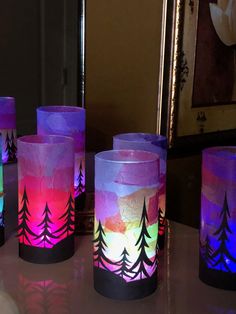 four lit candles with trees painted on them sitting on a table in front of a mirror