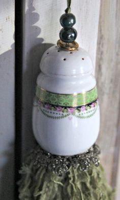 a white jar with green and gold trim hanging from a hook