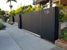 a black fence on the side of a sidewalk next to a building with trees and bushes