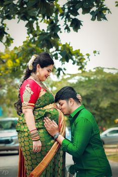 a man and woman standing next to each other in front of a tree with cars behind them