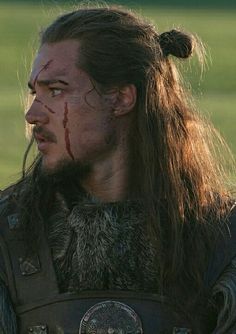 a close up of a person with long hair and blood on his face wearing armor