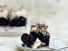 a piece of chocolate cake with white frosting on a plate next to a fork