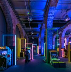 a room with arcade machines and neon colored lights on the walls, along with brick arches