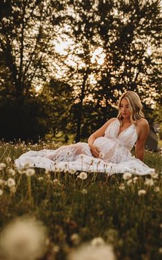 a woman is sitting on the grass in front of some trees