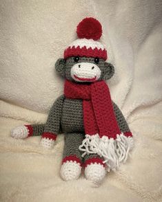 a crocheted sock monkey wearing a red and gray hat with a pom - pom