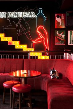 a dog sitting on the back of a red couch next to a table and stools