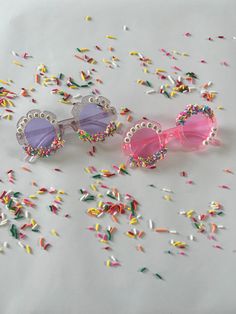 three pairs of pink sunglasses surrounded by confetti and sprinkles on a white surface