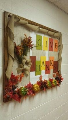 a sign that says give thanks hanging on the side of a wall with fall leaves