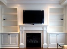 a living room with white bookcases and a flat screen tv above the fireplace