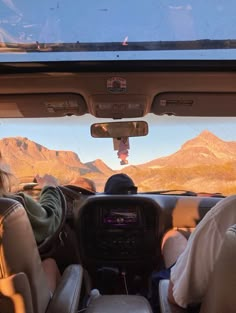 two people sitting in the passenger seat of a vehicle with mountains in the back ground