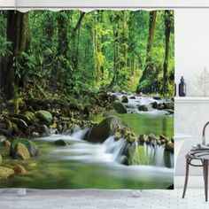 a bathroom with a shower curtain that has a river running through it in the woods