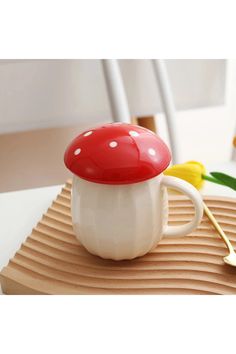 a red and white mushroom shaped coffee mug on top of a wooden table next to yellow tulips