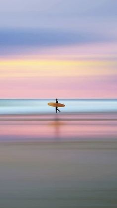 a man with a surfboard walking on the beach at sunset in front of the ocean