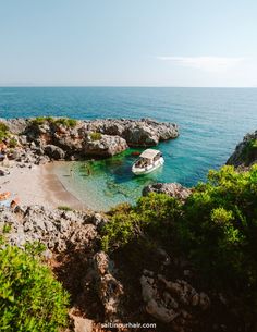 a small boat is in the water near some rocks and plants on the shore line