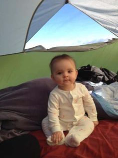 a baby sitting on top of a bed next to a tent