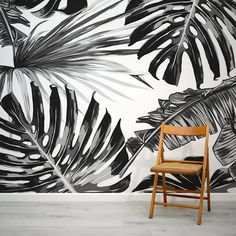 a chair sitting in front of a wall with black and white palm leaves on it