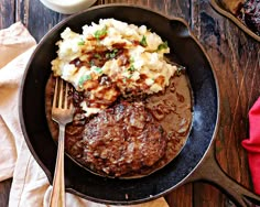 a skillet with mashed potatoes, meat and gravy on it next to a glass of milk