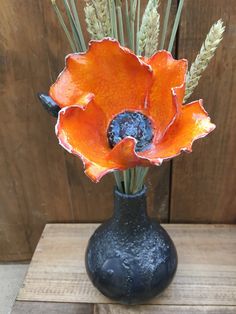 an orange flower in a black vase on a wooden table