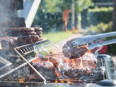 hamburgers being grilled on the grill with tongs