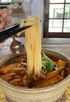 someone is holding chopsticks above a bowl of noodles