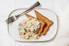 a white plate topped with two pieces of bread next to a bowl of chicken salad