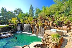 an outdoor swimming pool with waterfall and hot tub in the middle, surrounded by lush green trees