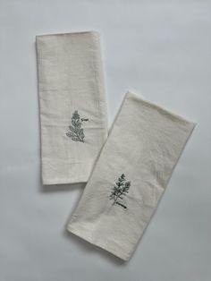 two white linen napkins with embroidered flowers and leaves on them, sitting side by side