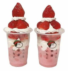 two plastic cups with strawberries and whipped cream in them on a plate next to a spoon