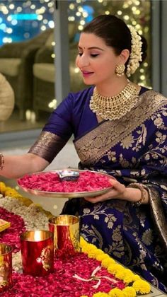 a woman in a blue and gold sari holding a plate with flowers on it