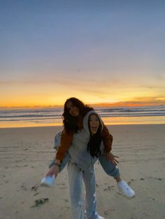 two girls are playing on the beach with their arms around each other as the sun sets