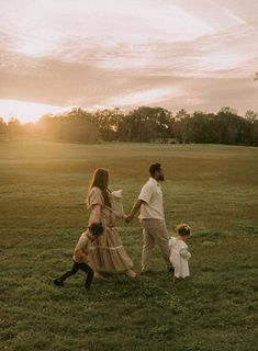 a man and woman holding hands while walking through a field with two small children in front of them