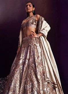 Introducing the stunning Gold Sequins Embroidered Bridal Lehenga Set is an exquisite blend of traditional elegance and modern sophistication. Crafted from luxurious tissue fabric, this gold lehenga showcases meticulous craftsmanship with its rich embellishments of gold and antique sequins, crystals, and bugle beads. The voluminous lehenga skirt flows effortlessly, exuding grace and grandeur. Paired with a matching embellished blouse offers a flattering, tailored fit. Completed with a delicate dupatta that drapes elegantly over the shoulders, adding a touch of ethereal charm. Perfect for the bride or bride-to-be, this lehenga set is designed to make you dazzle on your special day, ensuring every moment is captured in timeless beauty. Composition : Lehenga, Blouse and Dupatta - Tissue Care: Fitted Kundan Gown With Intricate Embroidery, Reception Sets With Intricate Embroidery, Fitted Sets With Mirror Work For Transitional Season, Transitional Gold Lehenga With Mirror Work, Fitted Wedding Sets With Mirror Work, Fitted Lehenga With Intricate Embroidery For Reception, Intricate Embroidered Fitted Lehenga For Reception, Festive Fitted Lehenga With Intricate Embroidery, Fitted Lehenga With Mirror Work For Reception