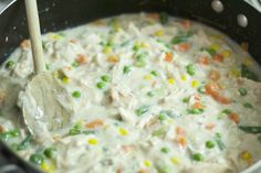 a pot filled with chicken and vegetables being stirred by a wooden spatula on the stove