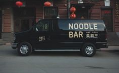 a black van parked in front of a building with red lanterns hanging from it's roof