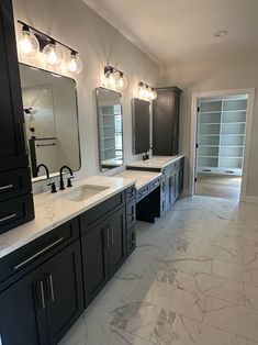 a large bathroom with double sinks, mirrors and lights on the wall above them is shown