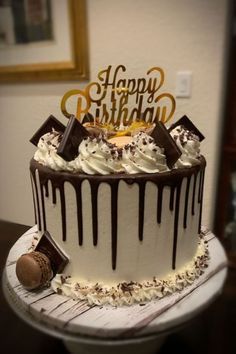 a birthday cake with white frosting and chocolate drizzled on top is sitting on a table