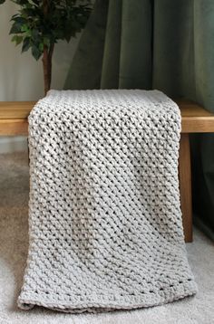 a white knitted blanket sitting on top of a wooden bench next to a potted plant