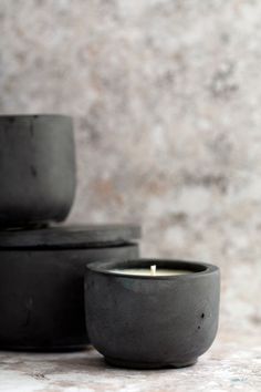 three black bowls sitting next to each other on top of a white countertop with a lit candle in the middle