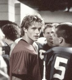 two young men standing next to each other in front of a group of football players