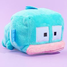 a blue and pink stuffed animal with eyes on it's head, sitting against a purple background