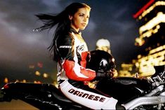 a woman sitting on top of a motorcycle in front of a cityscape at night