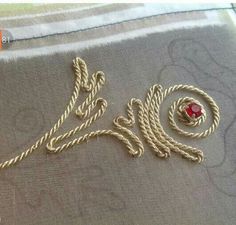 a piece of cloth with gold thread and a red bead on the end, sitting on a table