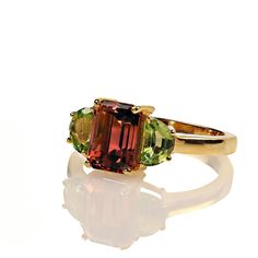 This is part of Chairish’s Fine Jewelry assortment.  Discover the rare beauty of this stunning Orange Tourmaline ring, accented with twin half-moon Peridots, all set in luxurious gold rhodium over sterling silver. This 2.70ct sparkling orange Tourmaline, sourced from the mountains outside of Rio de Janeiro, boasts a coveted, fiery hue that makes it truly exceptional. The vibrant green Peridots perfectly complement the warm orange tone of the Tourmaline, creating a breathtaking contrast that enha Elegant Three Stone Tourmaline Jewelry, Orange Tone, Rare Beauty, Peridot Ring, Green Peridot, Tourmaline Ring, Vibrant Green, Half Moon, Rio De Janeiro