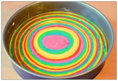 a metal bowl filled with multicolored cake batter on top of a wooden table