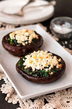 two stuffed mushrooms with cheese and spinach on a white plate next to silverware