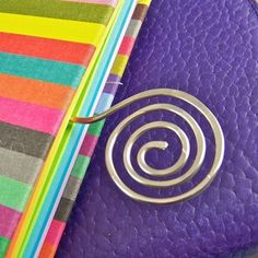 a purple purse with a spiral design on the front and side, next to a multicolored wallet