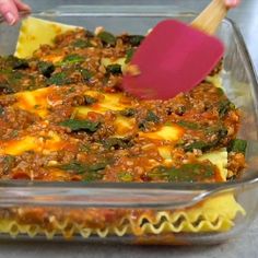 a casserole dish with meat and vegetables being stirred by a red spatula